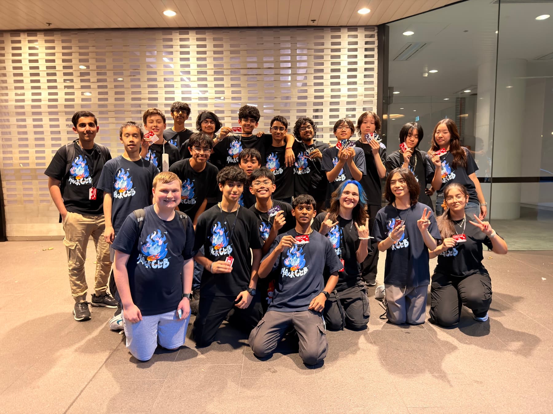 A large group of teenagers in matching shirts posing together at a hackathon