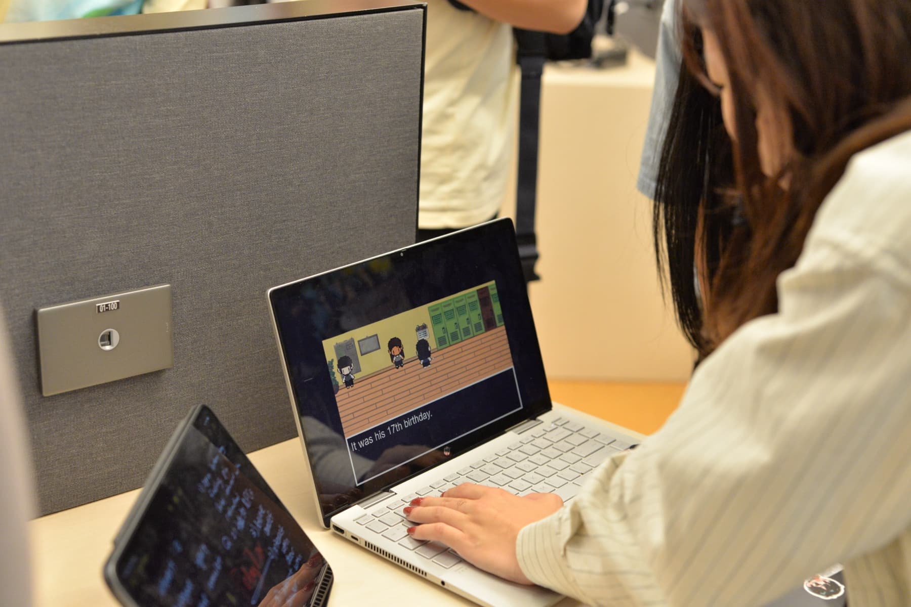 A teenager working at a laptop showing a pixel-art game scene